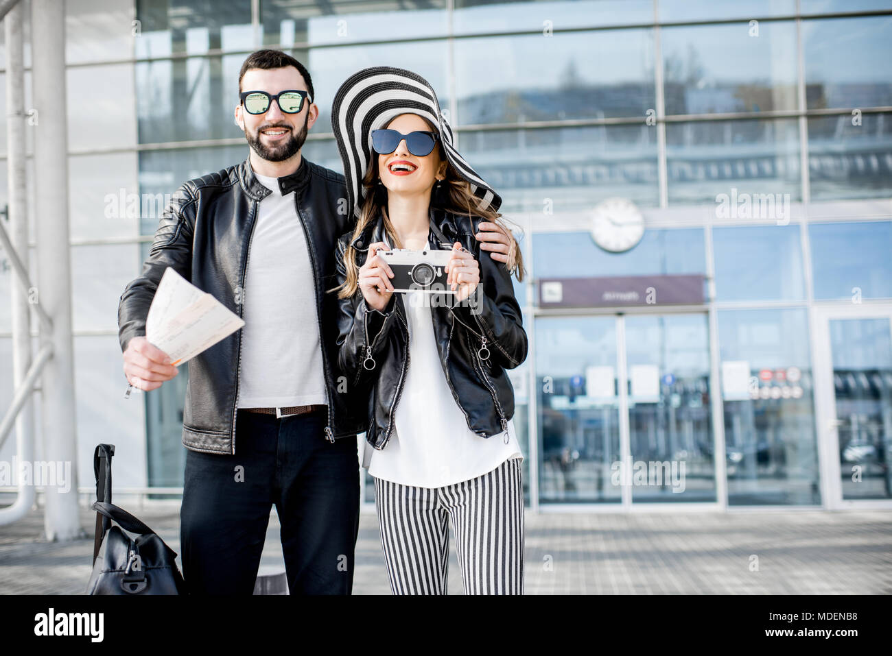 Porträt eines jungen Paares in Lederjacken stehen mit Tickets und Gepäck in der Nähe des Flughafen Terminals während der Flitterwochen Stockfoto