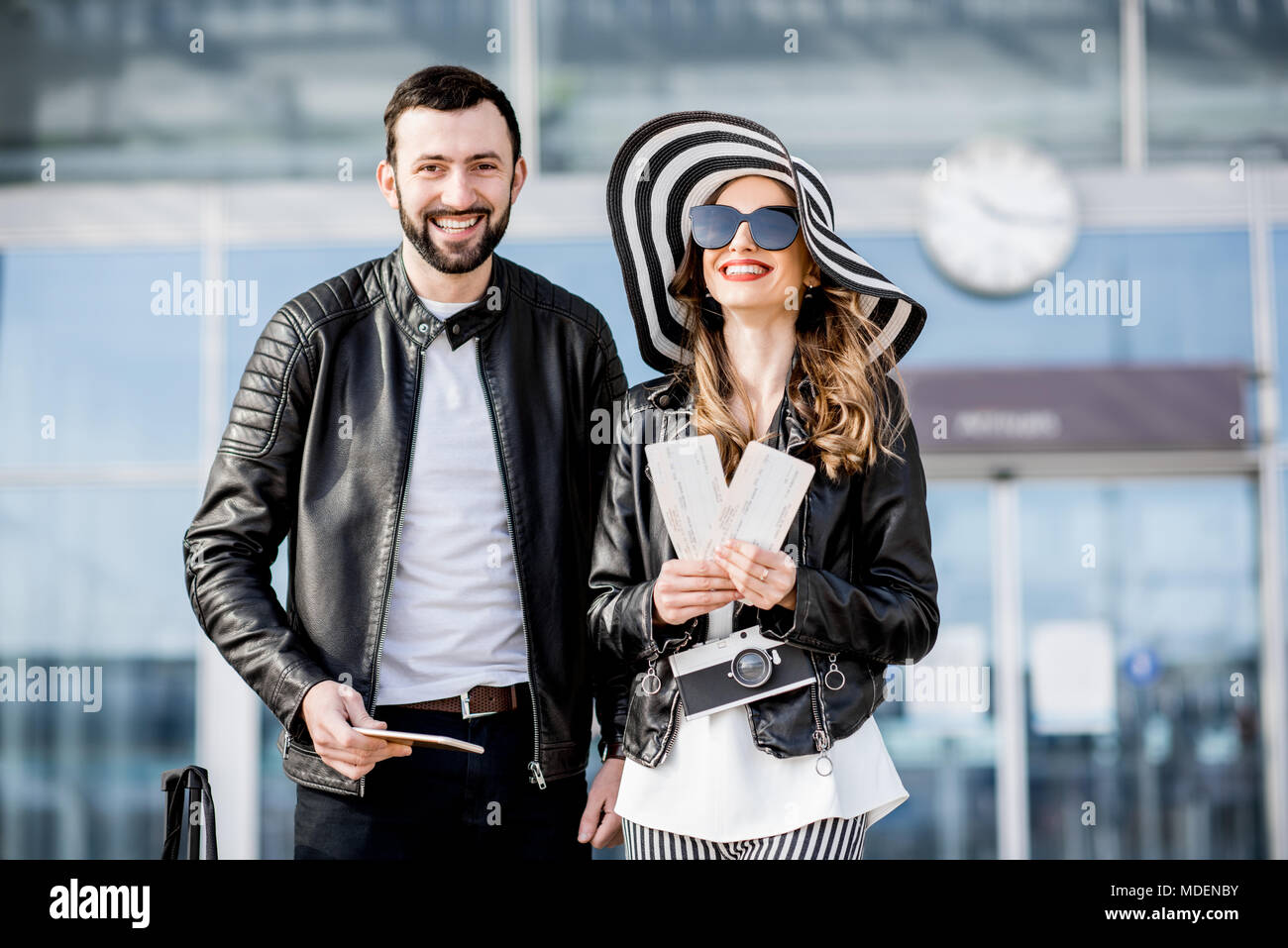 Porträt eines jungen Paares in Lederjacken stehen mit Tickets und Gepäck in der Nähe des Flughafens während der Flitterwochen Stockfoto