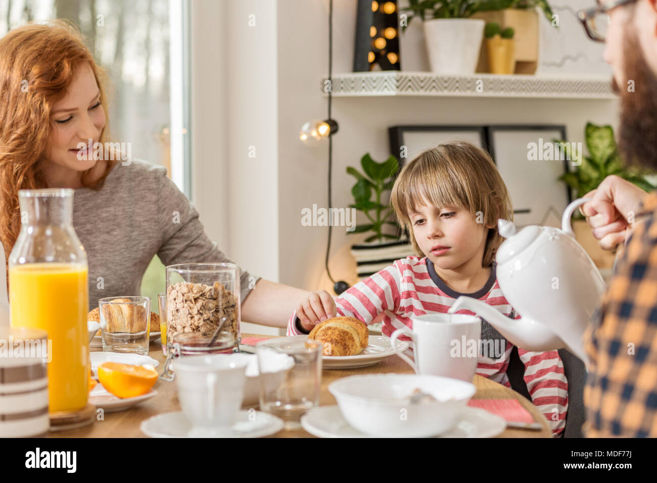 Schöne Mutter überzeugend ihrem Sohn Brot für das Frühstück zu essen Stockfoto