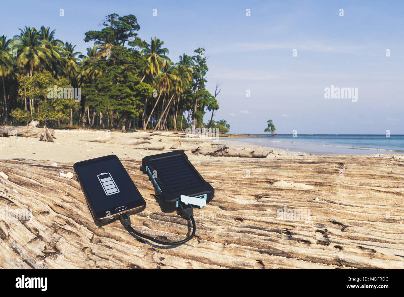 Akku Solar Energy Device auf einem Hintergrund der Sandstrand von einer unbewohnten Insel. Smart Phone aus der Solar Batterie. Die Solar Batterie Stockfoto