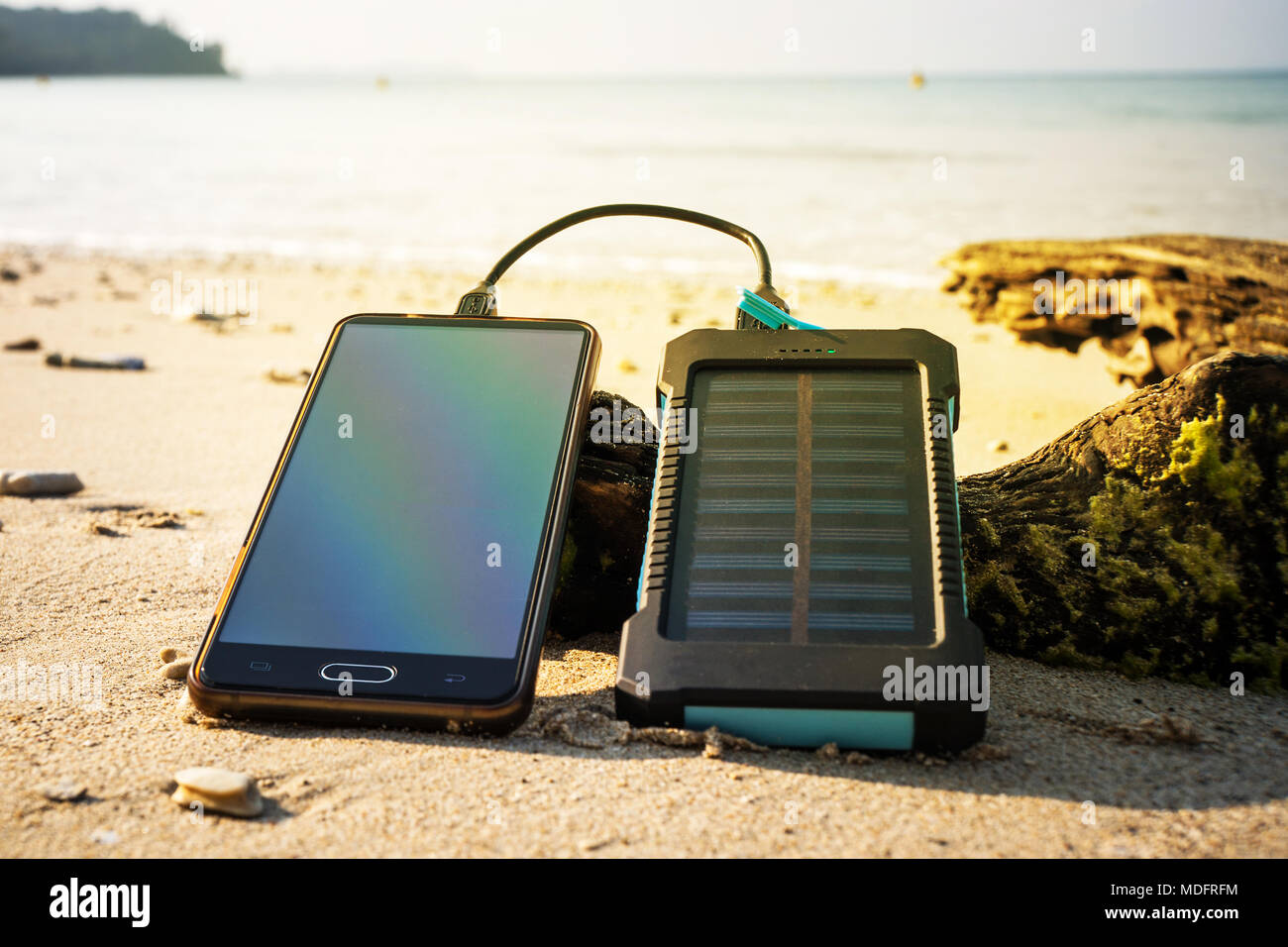 Akku Solar Energy Device auf einem Hintergrund der Sandstrand von einer unbewohnten Insel. Smart Phone aus der Solar Batterie. Die Solar Batterie Stockfoto