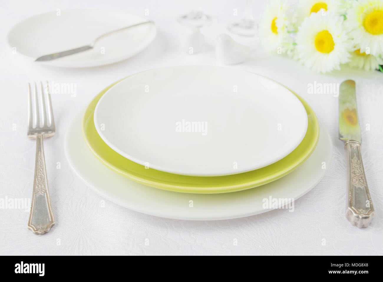 Classic für ein Galadinner mit weißen und grünen Porzellan Teller, Besteck und Kamillenblüten auf einer weißen Tischdecke Stockfoto