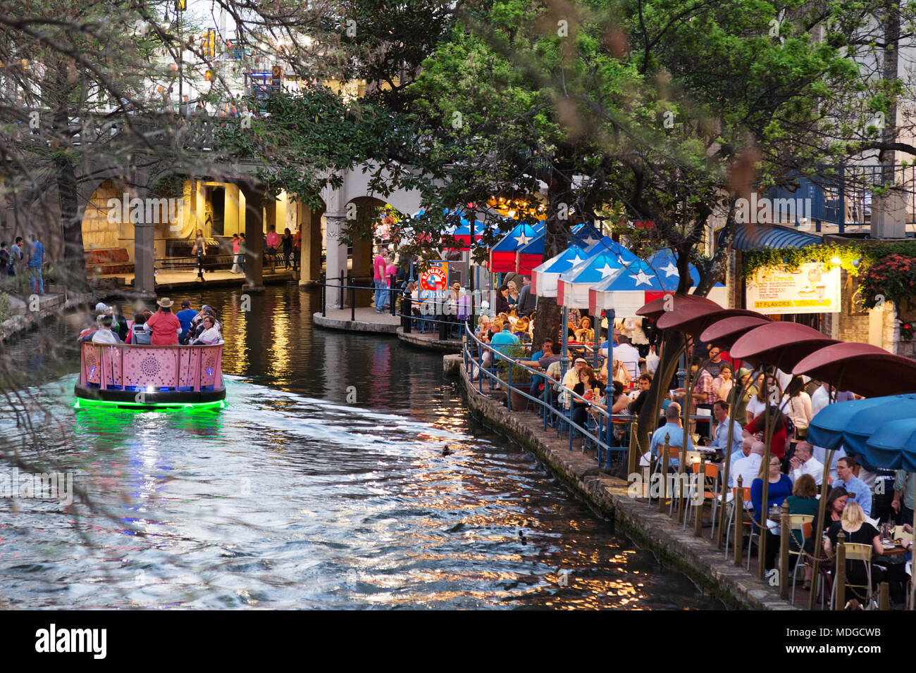 San Antonio River Walk - ein touristenboot auf dem San Antonio River vorbei an Restaurants in der Dämmerung; die San Antonio Riverwalk San Antonio, Texas, USA Stockfoto
