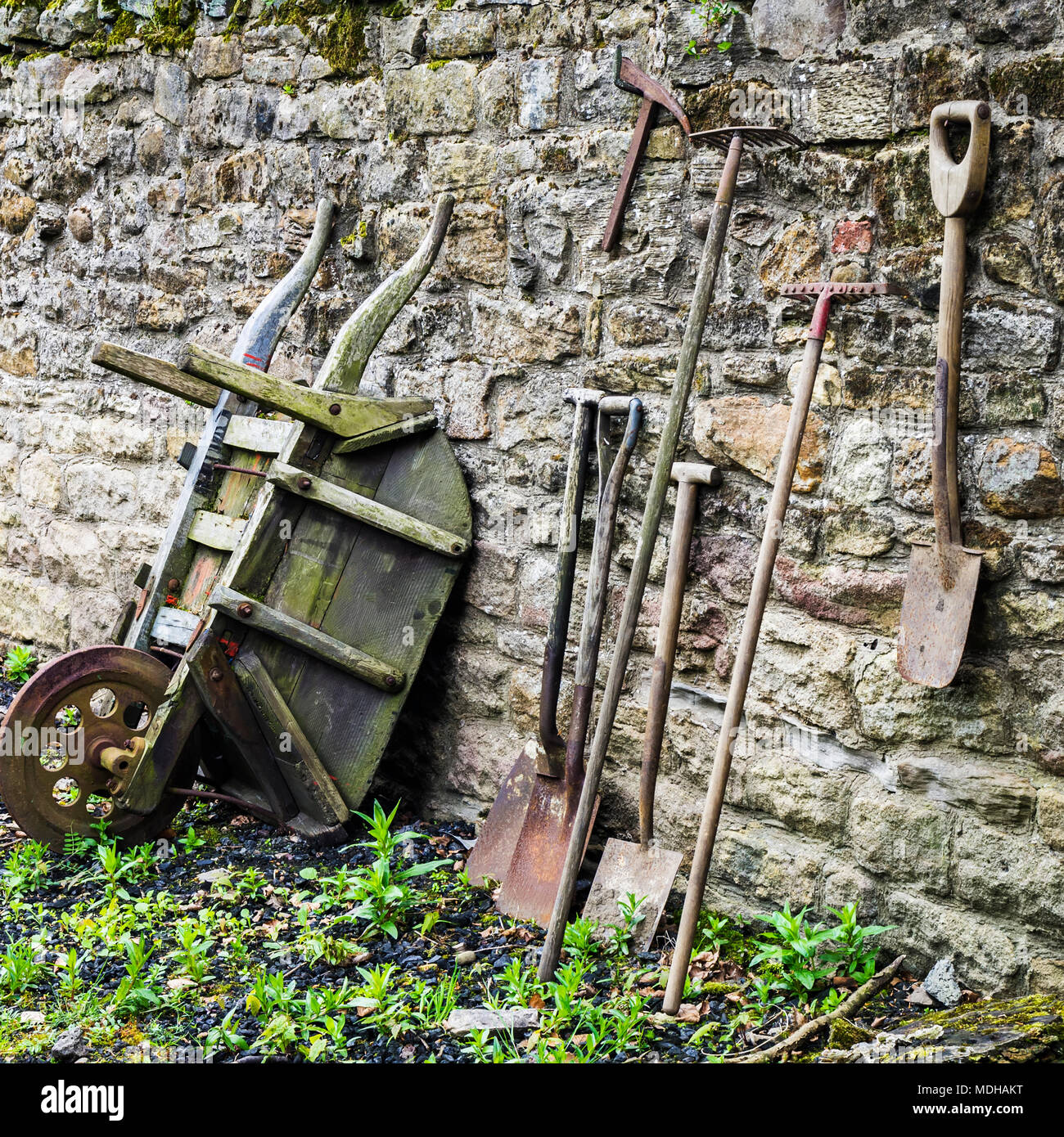 Alte Garten Werkzeuge lehnte sich gegen einen Verwitterten stein Wand, das Open Air Museum, England Stockfoto