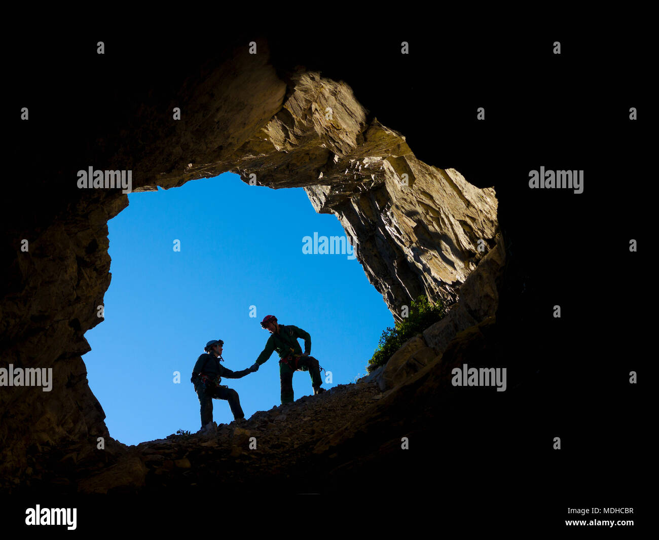 Ein junges Paar, das Klettern im Mund der Höhle, Hände halten für Unterstützung; Fernie, British Columbia, Kanada Stockfoto