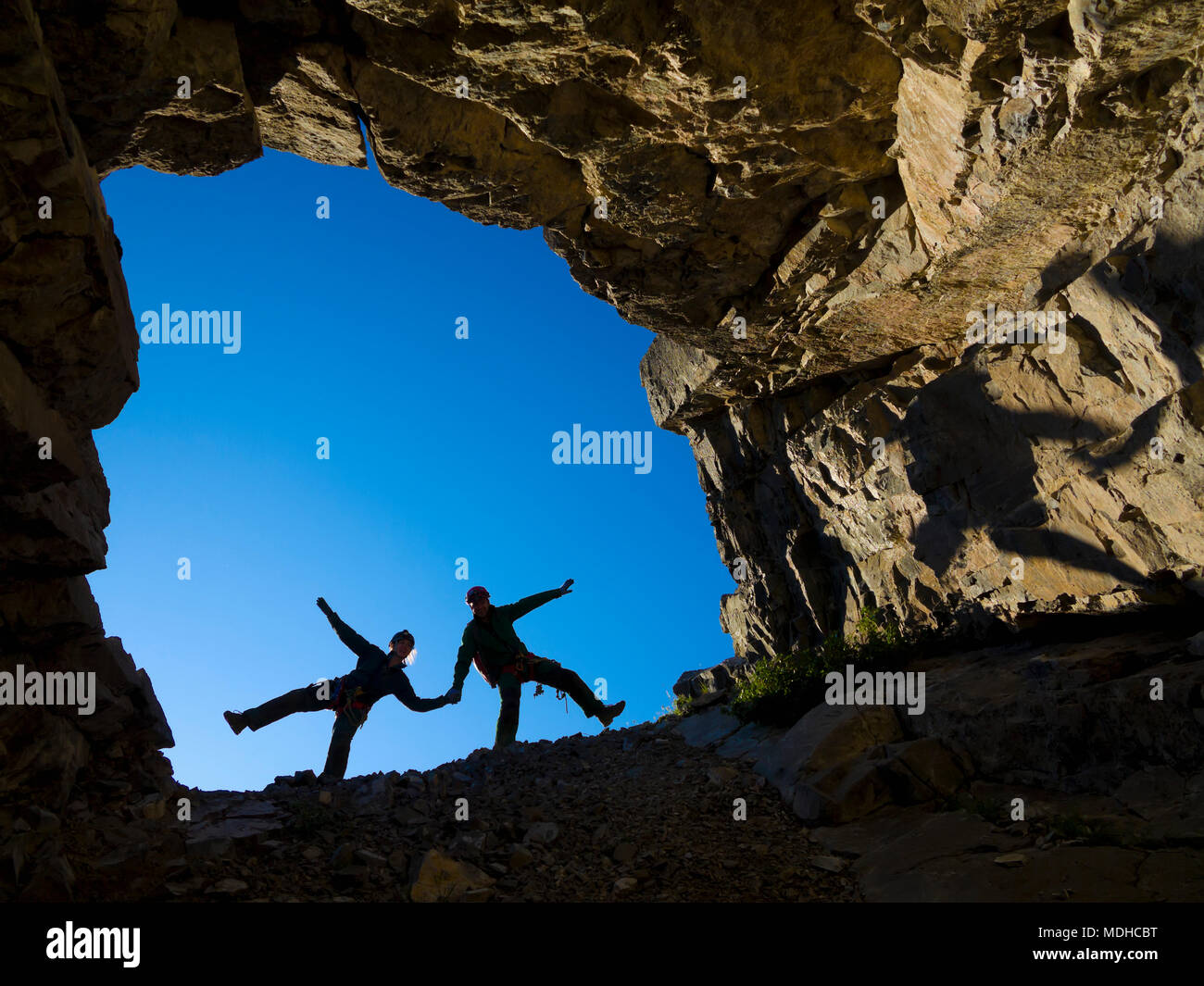 Ein junges Paar, das Klettern im Mund der Höhle, Hände halten und Sein playful, Fernie, British Columbia, Kanada Stockfoto