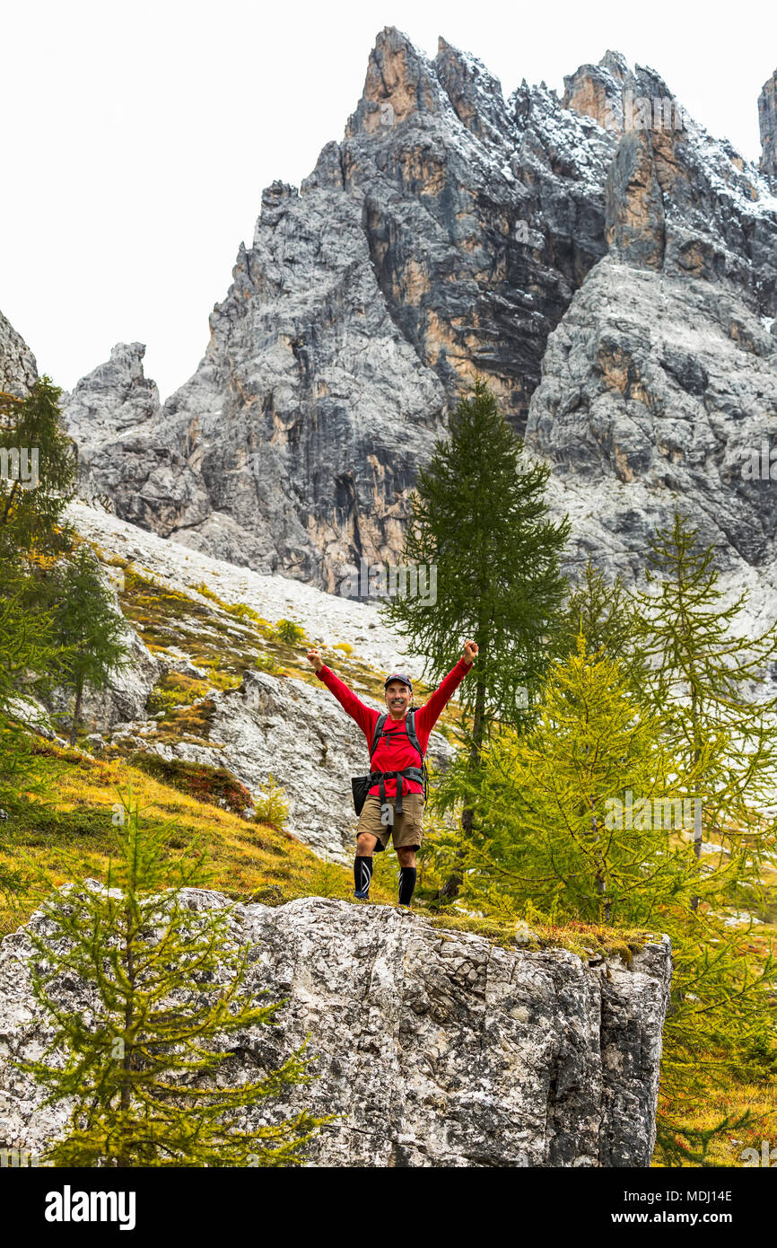 Männliche Wanderer mit Arme oben auf großen Felsen mit felsigen Hang und Berg; Sesto, Bozen, Italien Stockfoto