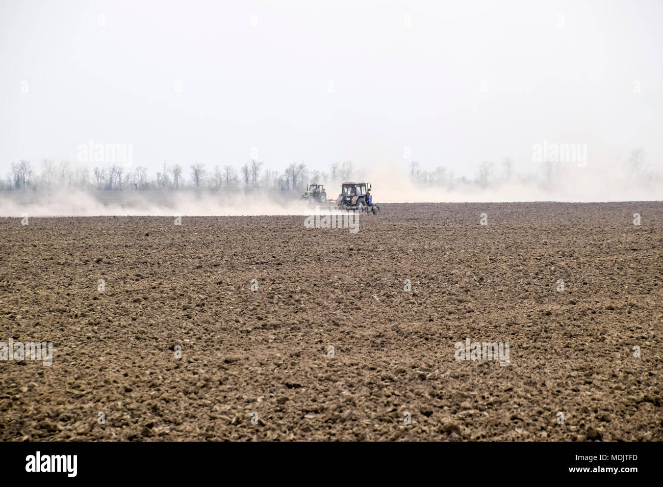 Der Traktor Eggen der Boden, auf dem Feld und schafft eine Staubwolke hinter sich. Stockfoto