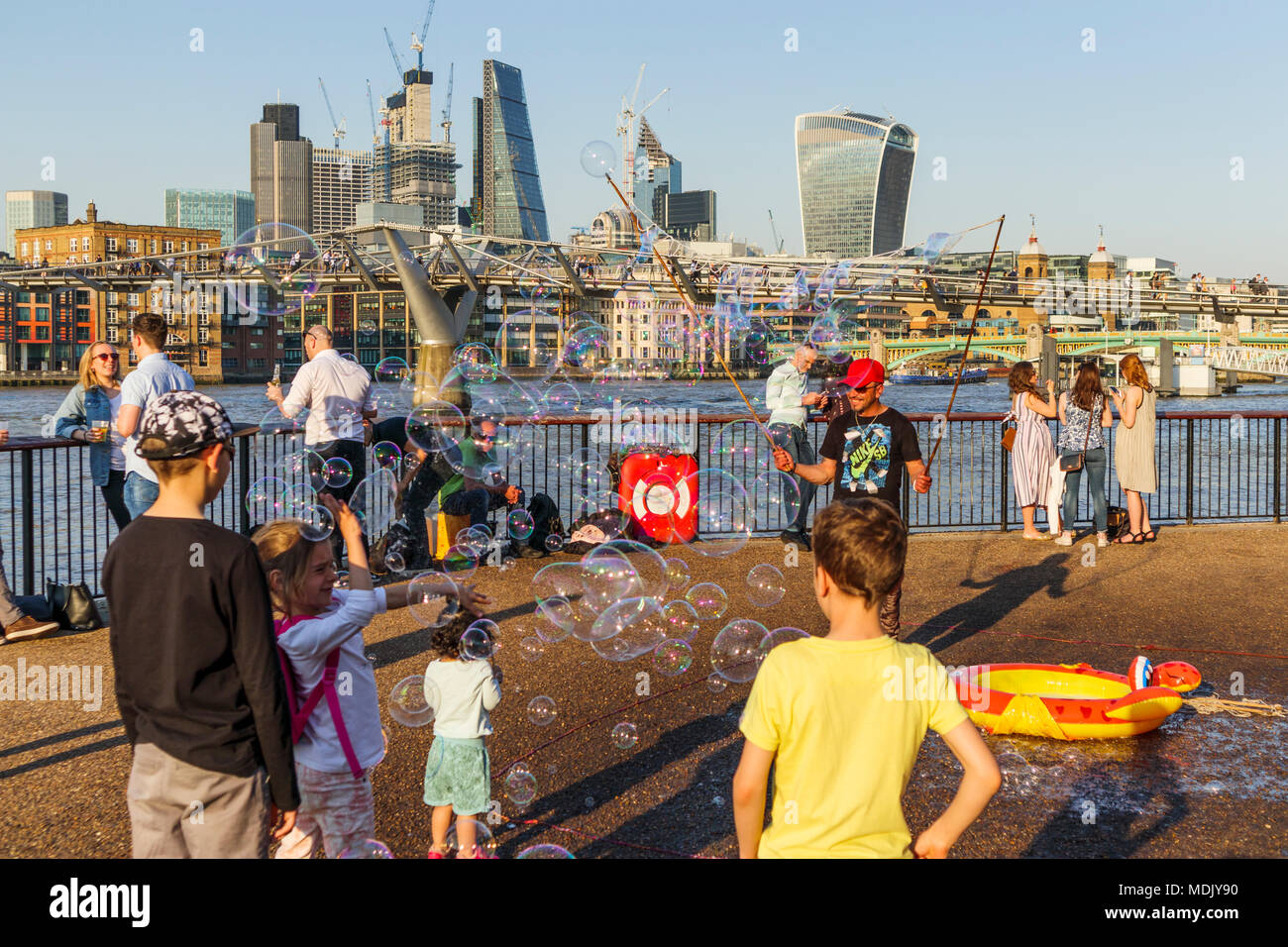 London, UK, 19. April 2018. Ein Entertainer am Südufer der Ufer der Themse in Bankside bläst Seifenblasen Kinder gegen eine Skyline Hintergrund von Ikonischen moderne Wolkenkratzer Gebäude in der Stadt London zu unterhalten. Die Sonnige schönem Wetter auf den wärmsten April Tag seit Jahrzehnten brachten gutmütige Massen, die Sonne zu genießen. Credit: Graham Prentice/Alamy Leben Nachrichten. Stockfoto