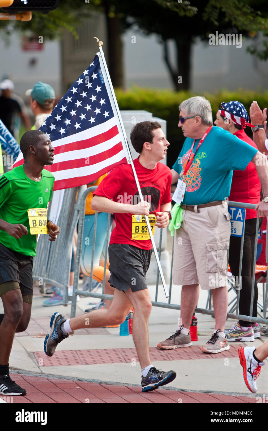 Ein Läufer trägt einen großen amerikanischen Flagge und gleichzeitig auf die Ziellinie in die Peachtree Road Race läuft am 4. Juli 2014 in Atlanta, GA. Stockfoto