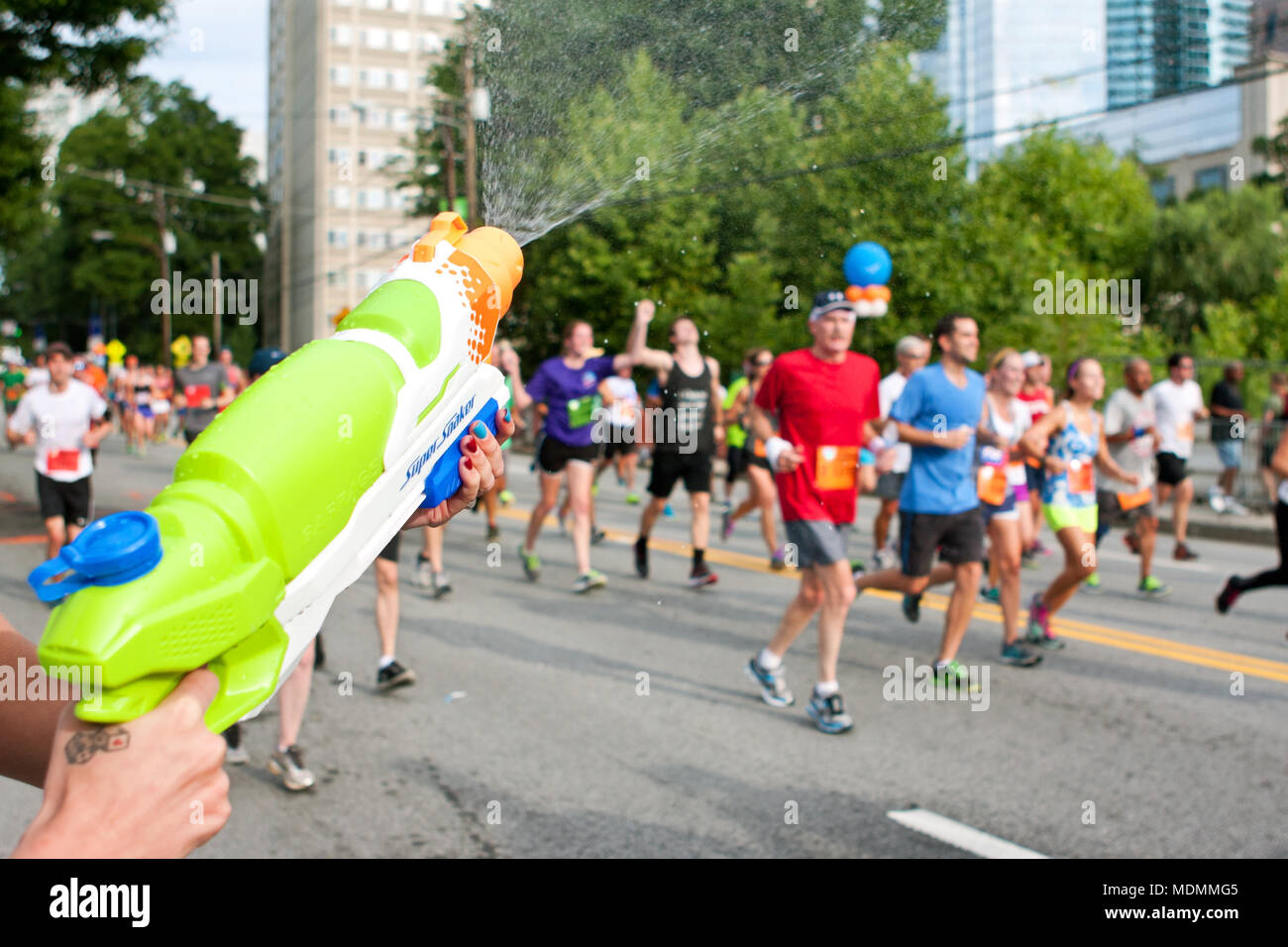 Atlanta, GA, USA - Juli 4, 2014: eine Frau zieht Läufer mit einem Spritzer Pistole, als sie auf dem Weg zur Ziellinie der Peachtree Road Race Kopf. Stockfoto
