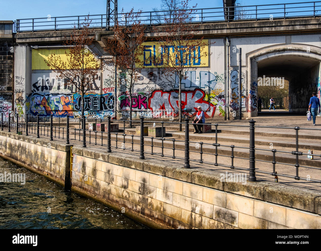 Berlin Mitte, Graffiti bedeckt Eisenbahnviadukt mit Fußgänger-Unterführung an der Spree mit Frau sitzt in der Sonne Stockfoto