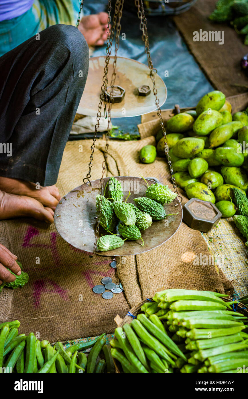 Lebensmittelhändler Verkäufer wiegen bitteren Kürbis in gemeinsamen Gleichgewicht für den Verkauf an Kunden in der indischen Supermarkt Stockfoto