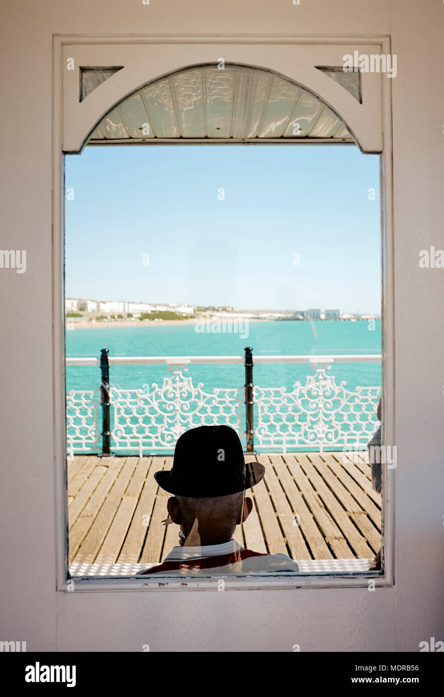 Ein Mann mit einem Trilby Hut sitzen auf den Brighton Pier im Sommer - ein aufgenommenen Szene an einem Sommertag in Brighton, England Stockfoto