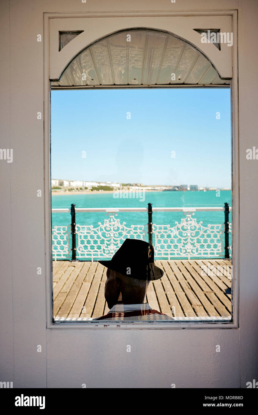 Ein Mann mit einem Trilby Hut sitzen auf den Brighton Pier im Sommer - ein aufgenommenen Szene an einem Sommertag in Brighton, England Stockfoto