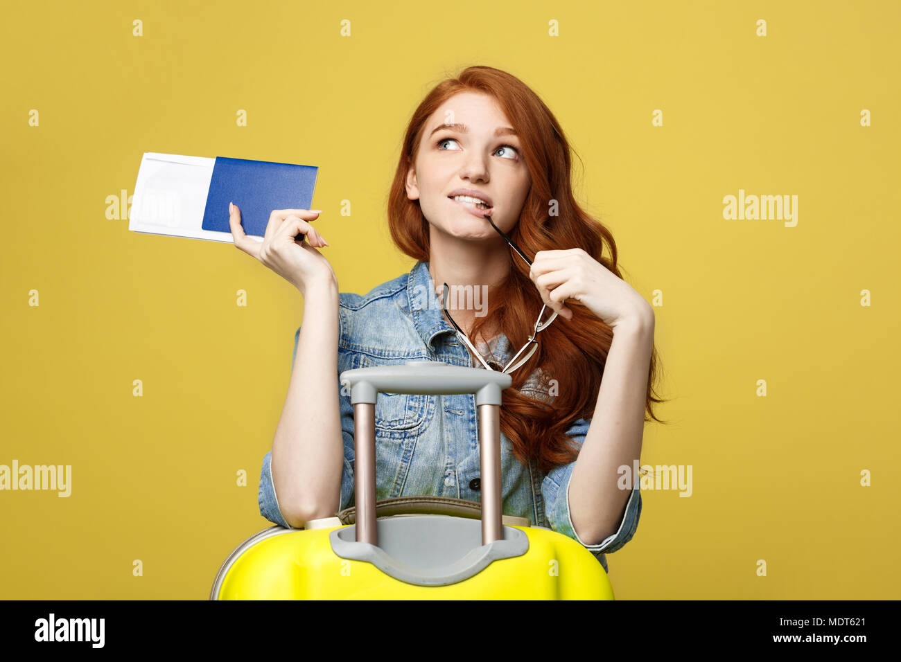 Travel Concept. Studio Portrait von hübsche junge Frau mit Reisepass und Glas mit Koffer und Denken über etwas. Auf weiß isoliert. Stockfoto
