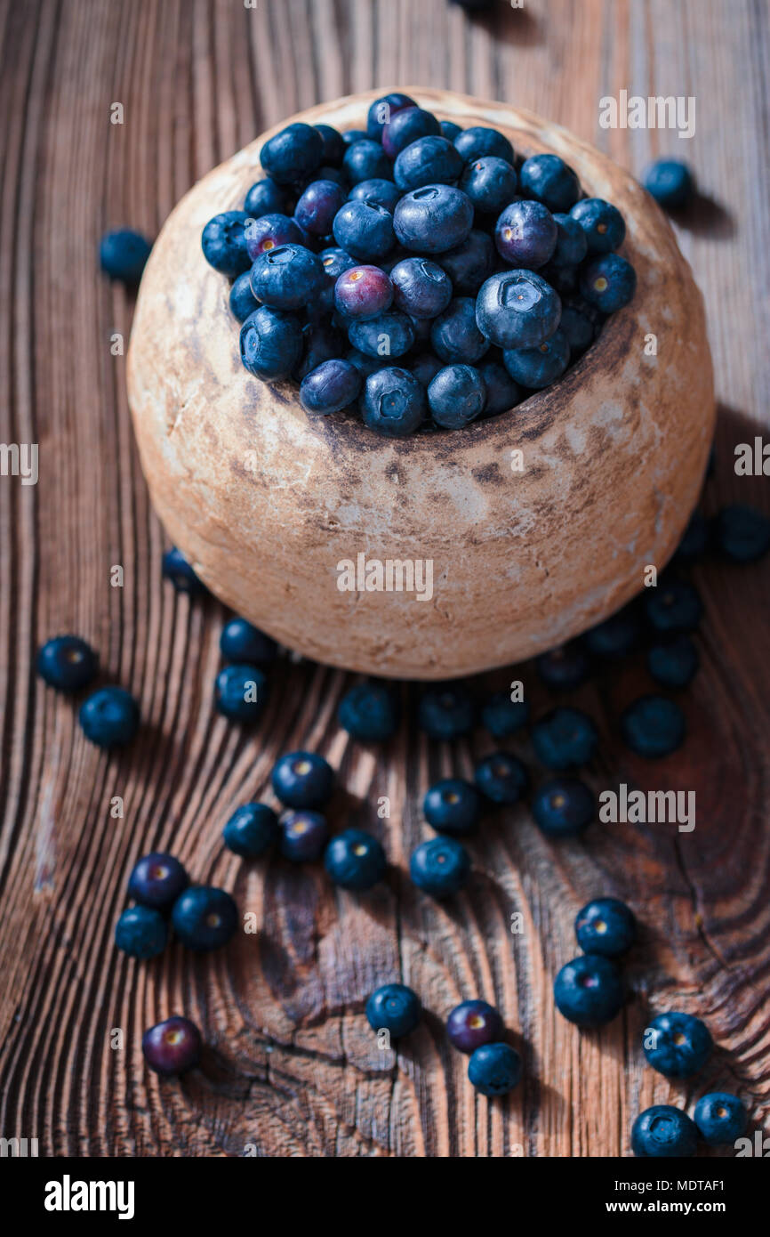 Frisch Blaubeeren in alte Keramik Schüssel gesammelt. Einige Früchte frei auf alten hölzernen Tisch verstreut. Von oben geschossen Stockfoto