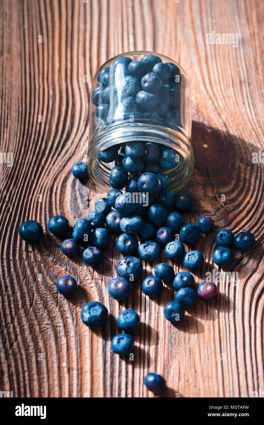 Frisch Blaubeeren in jar gestellt wurden. Einige Früchte frei auf alten hölzernen Tisch verstreut. Von oben geschossen Stockfoto