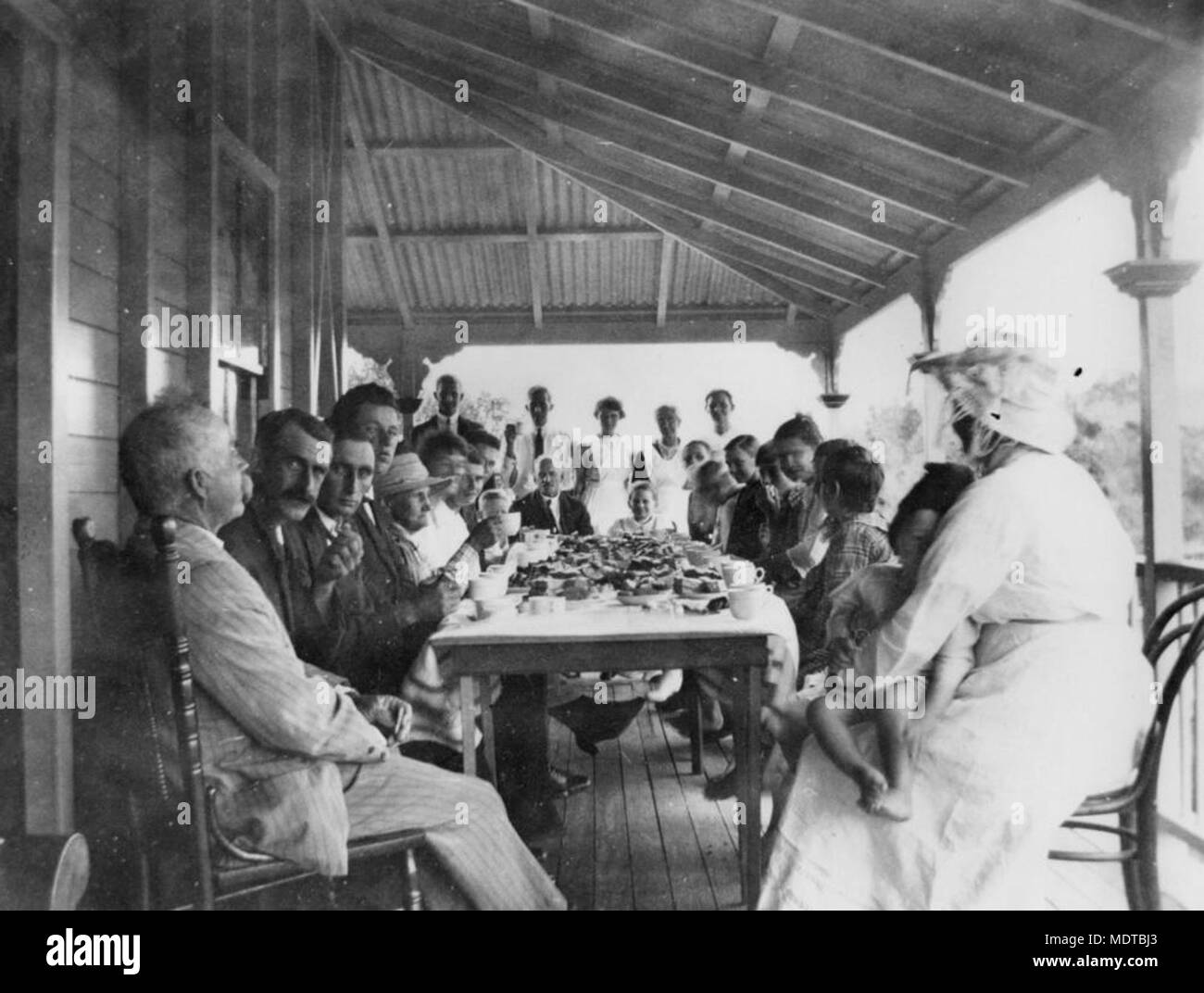 Mittagessen auf der Veranda von George Davis', Barneyview. Ort: Queensland, Australien Beschreibung: Ca. 25 Männer, Frauen und Kinder sind in einer Tabelle unter einer Veranda mit einem Mittagessen, sitzt, bereit zu essen. Stockfoto