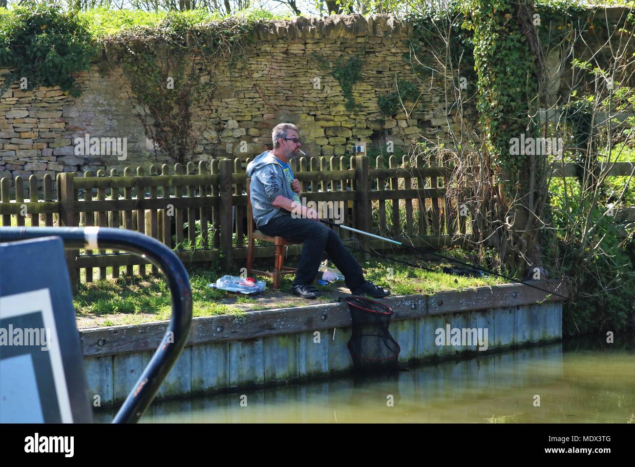 Weiß im mittleren Alter Mann mit Zigarette im Mund Angeln an der Seite des Kanals an der sonnigen Enslow Wharf, Bletchingdon, Oxfordshire Stockfoto