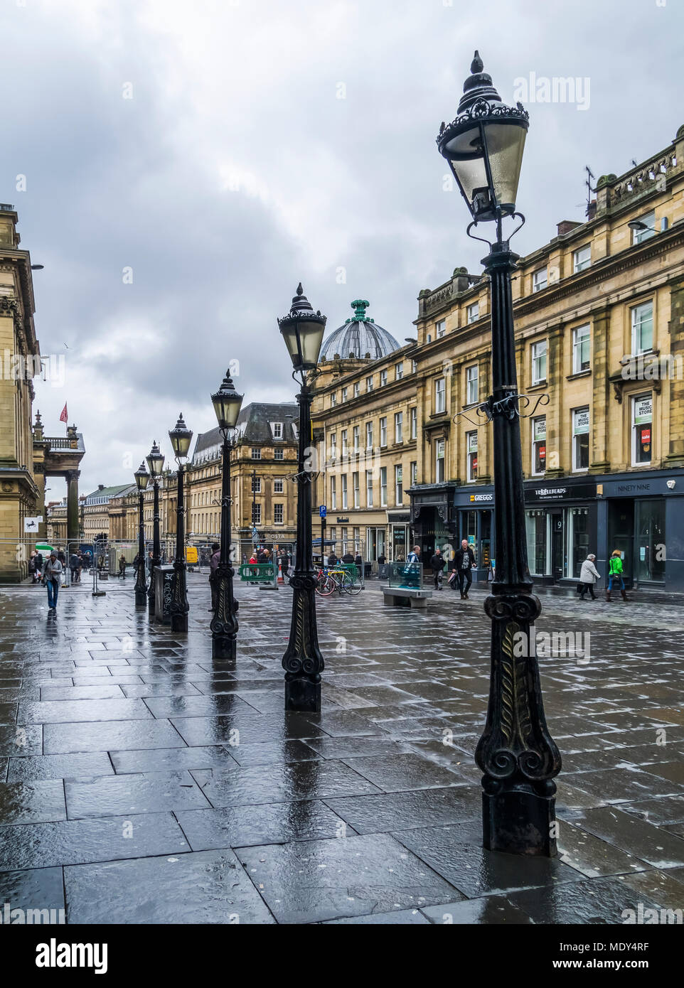 Dekorative lampe Beiträge in einer Reihe entlang einer nassen Straße mit Fußgängern und Geschäfte, Newcastle Upon Tyne, Tyne und Wear, England Stockfoto