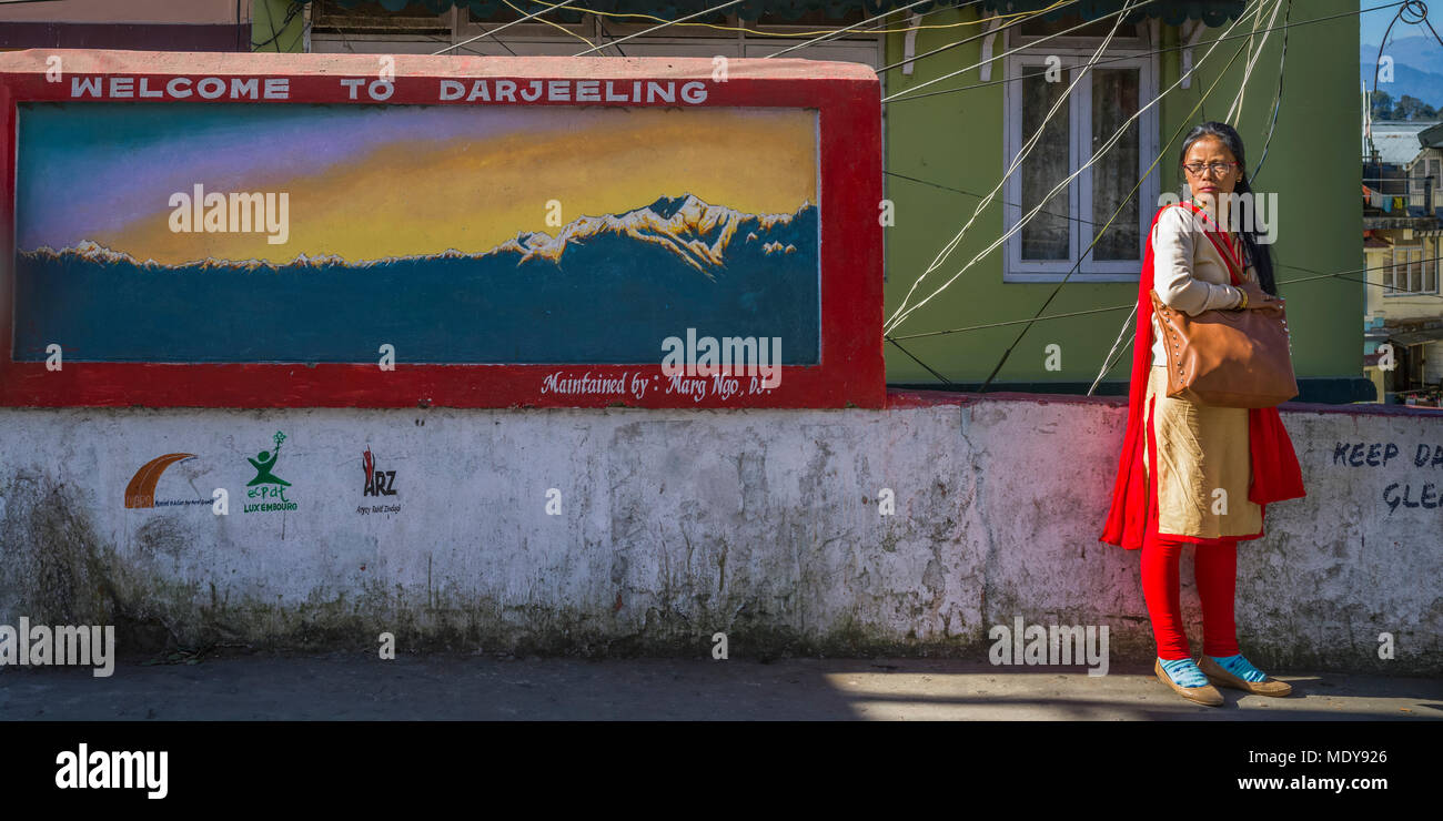 Eine indische Frau steht neben einer Wand mit einem Wandgemälde und ein Schild mit der Aufschrift "Willkommen in Darjeeling, Darjeeling, West Bengalen, Indien gemalt Stockfoto