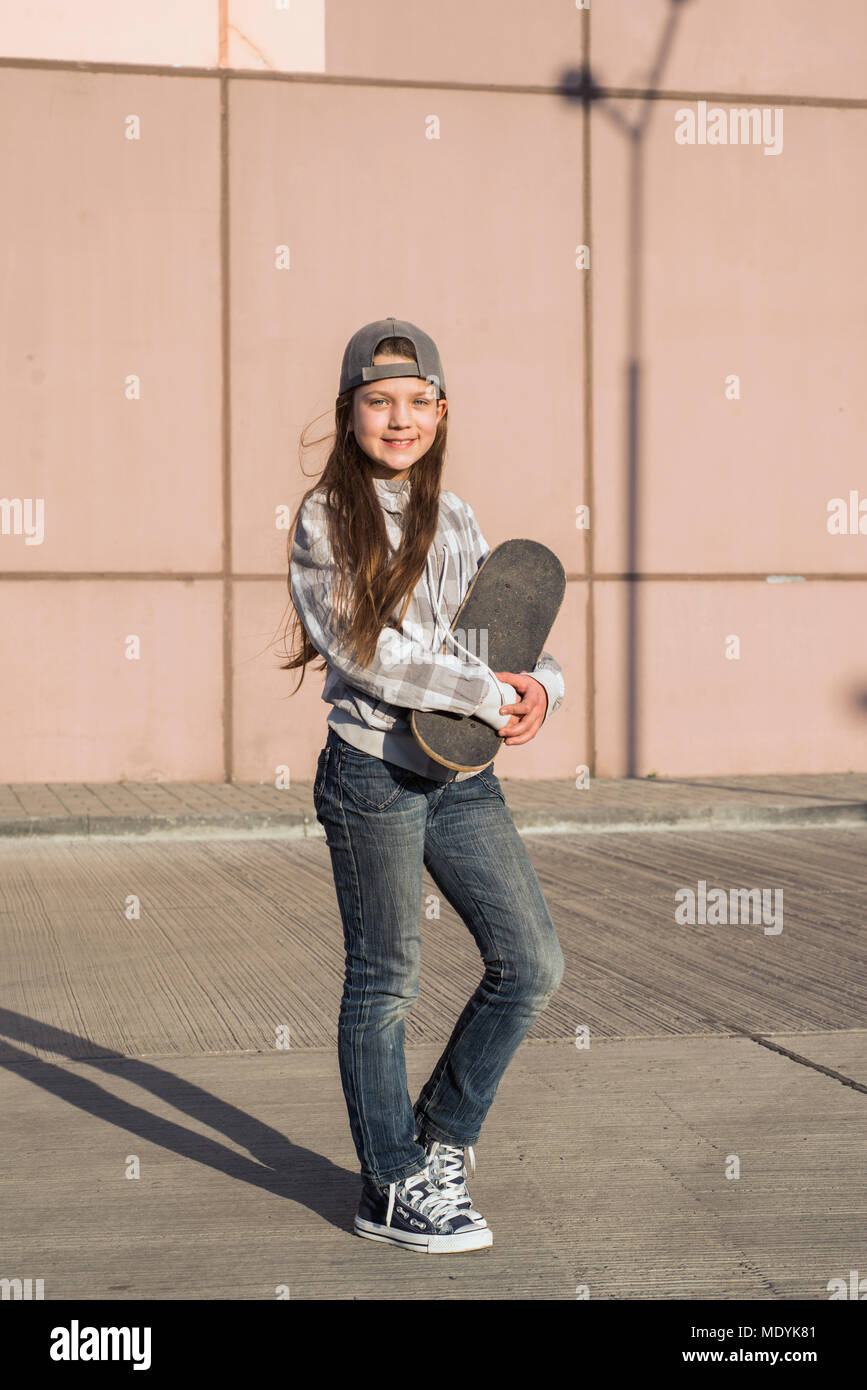 Urban Mädchen mit Skateboard posiert auf leeren Parkplatz mit Gebäude Wand hinter Stockfoto