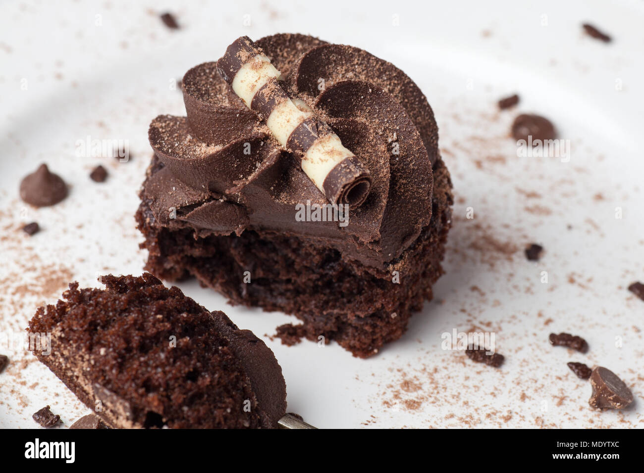 Chocolate Cupcake auf weißer Teller mit Gabel, bestäubt mit Kakao und Schokolade besprüht, die Hälfte gegessen Stockfoto