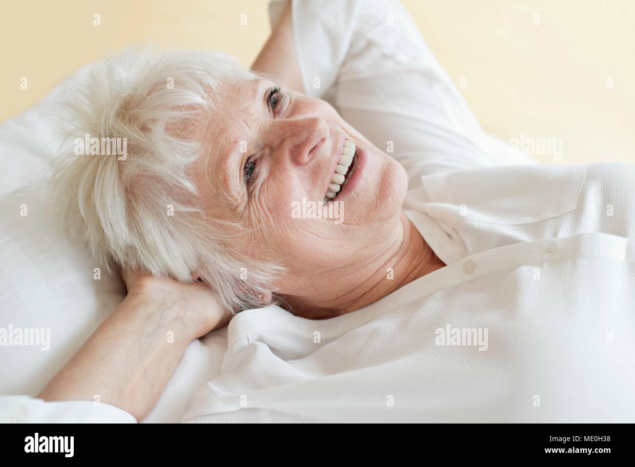 Ältere Frau liegend mit den Händen hinter dem Kopf. Stockfoto