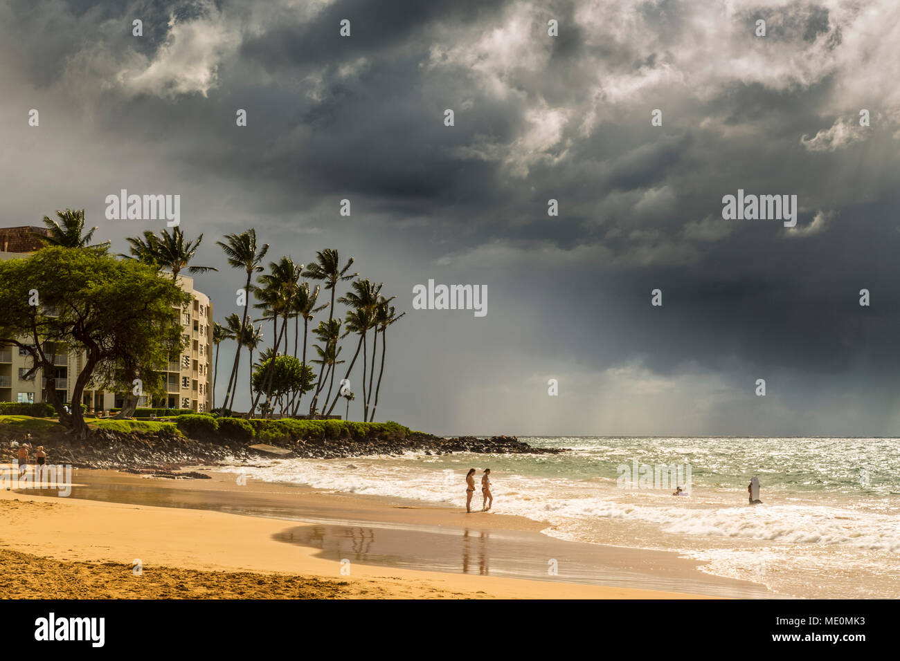 Touristen am Strand auf der Insel Maui mit dunklen Wolken und Niederschlag über dem Meer in der Ferne Stockfoto
