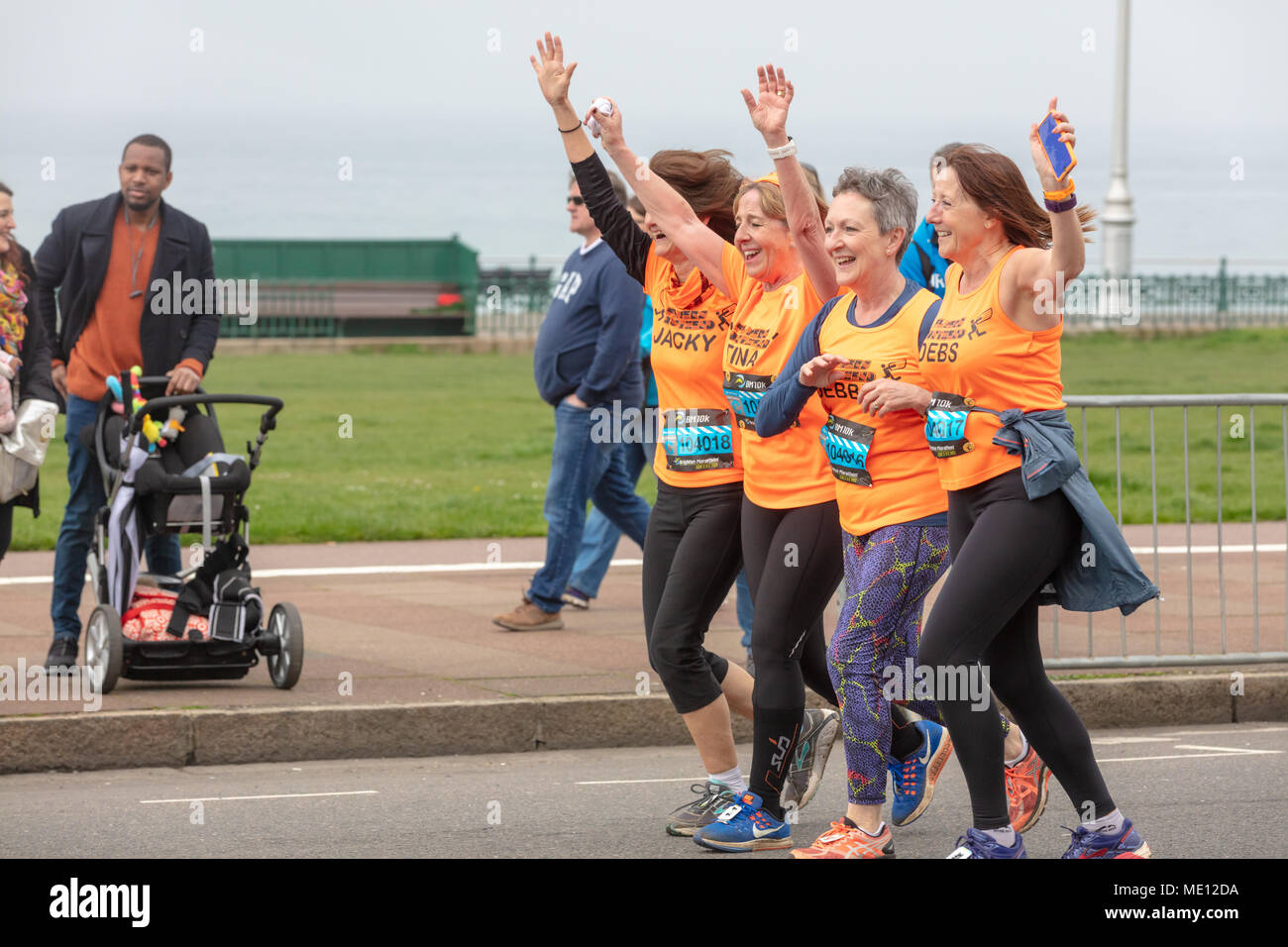 Brighton, Sussex, UK, 15. April 2018; vier Frauen, Orange Tops Lächeln und winken während der Teilnahme in Brighton 10 K Rennen Stockfoto