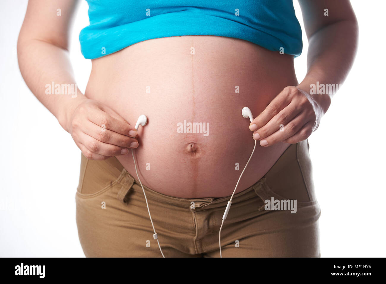 Ohrhörer in der Nähe von schwangeren Bauch auf weißem Hintergrund Stockfoto