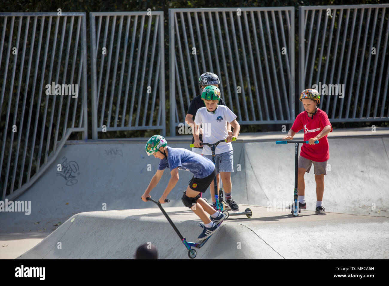 Junge Jungs mit Helmen fahren auf Rollern und Skateboards in einem Skatepark in Sydney, NSW, Australien Stockfoto