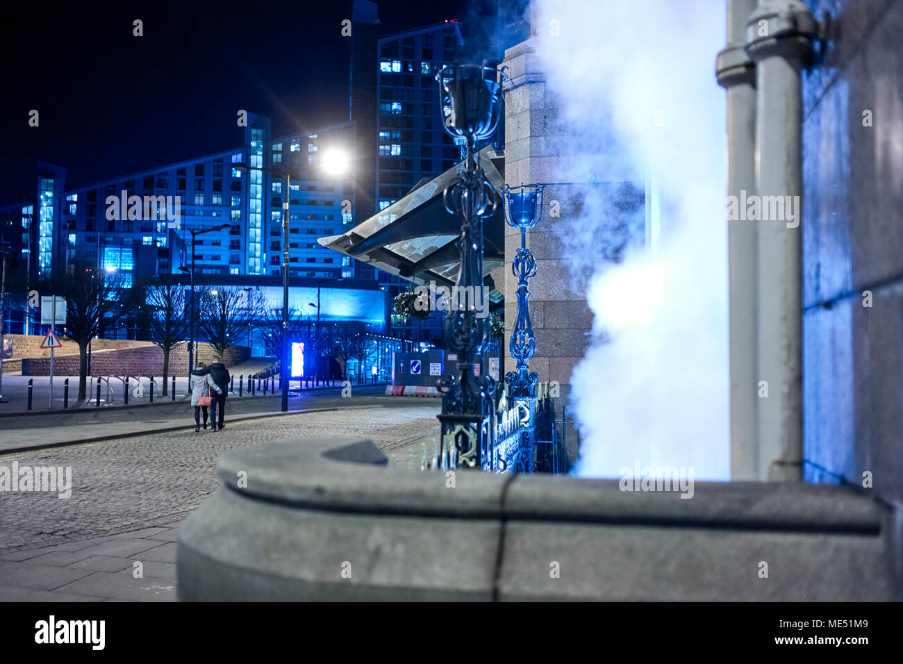 Ein junges Paar Spaziergang, vorbei an einem dampfenden Steckdose von einem Hotel im Zentrum von Manchester in einer kalten Winternacht Stockfoto