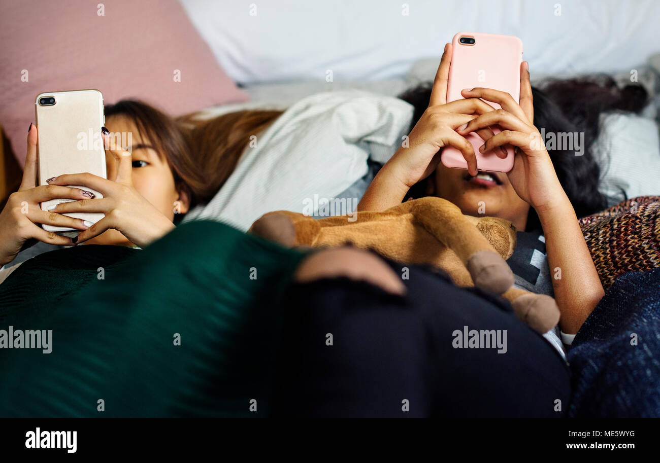 Mädchen im Teenageralter mit Smartphones auf einem Bett internet in Slumber Party Stockfoto