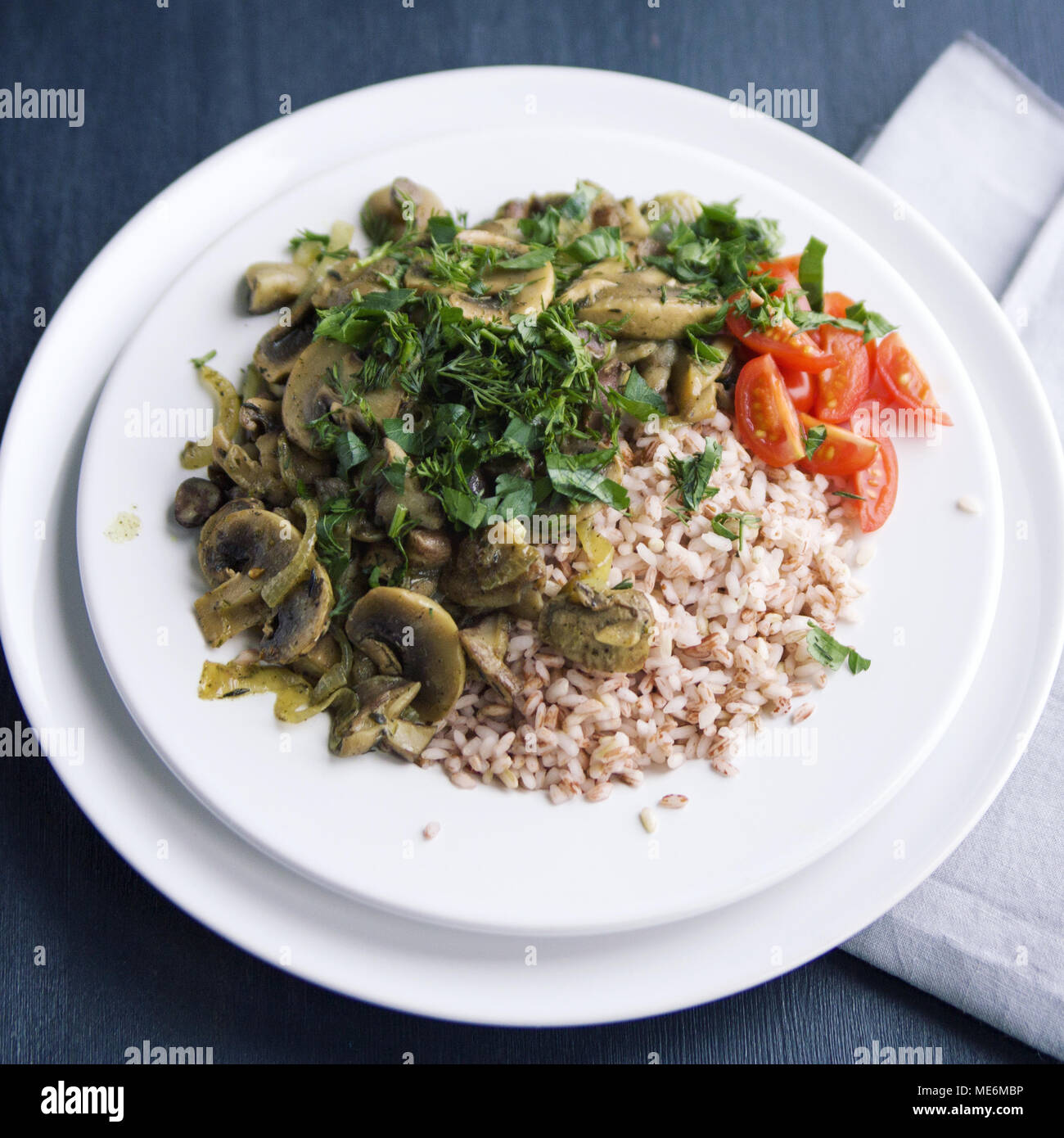 Roter Reis mit Pilzen und Tomaten. Vegane Gerichte. Europäische Küche. Einfach gesundes Mittagessen. Vegetarisches Reisgericht auf dem weißen Teller. Close Up. Zu Stockfoto