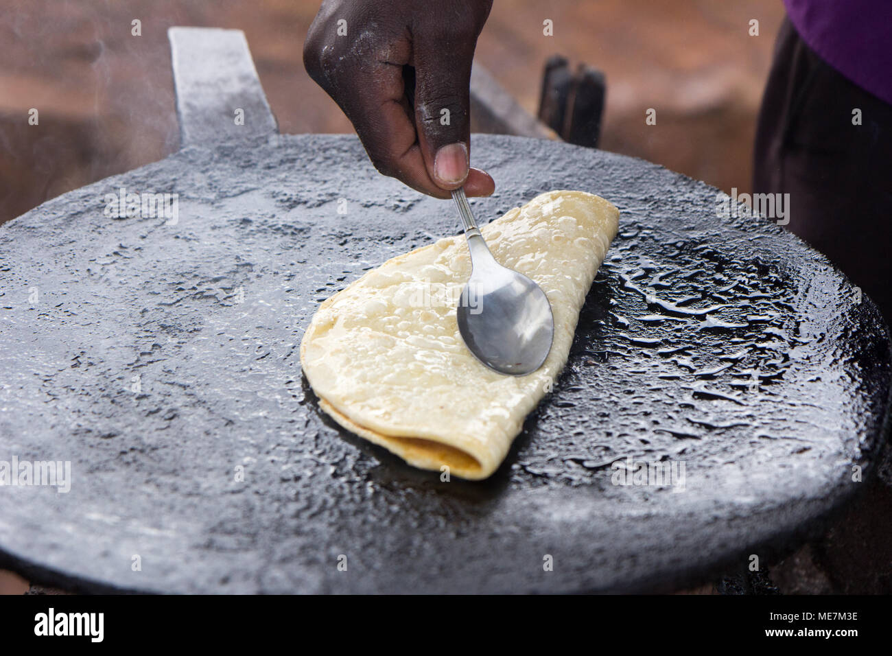 Ein fladenbrot "chapati" gebraten und mit einem Löffel durch eine native Ugandischen cook gefaltet. In Uganda im Mai 2017 erschossen. Stockfoto
