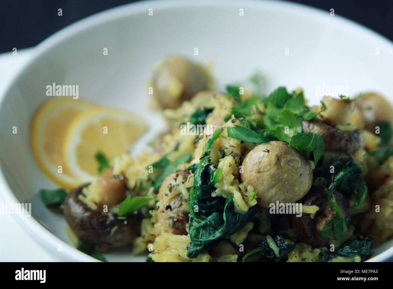 Gelber Reis mit Pilzen und Spinat. Vegane Gerichte. Europäische Küche. Vegetarische Gelbwurz Reis in die weiße Schüssel. Close Up. Getönten Foto. Stockfoto