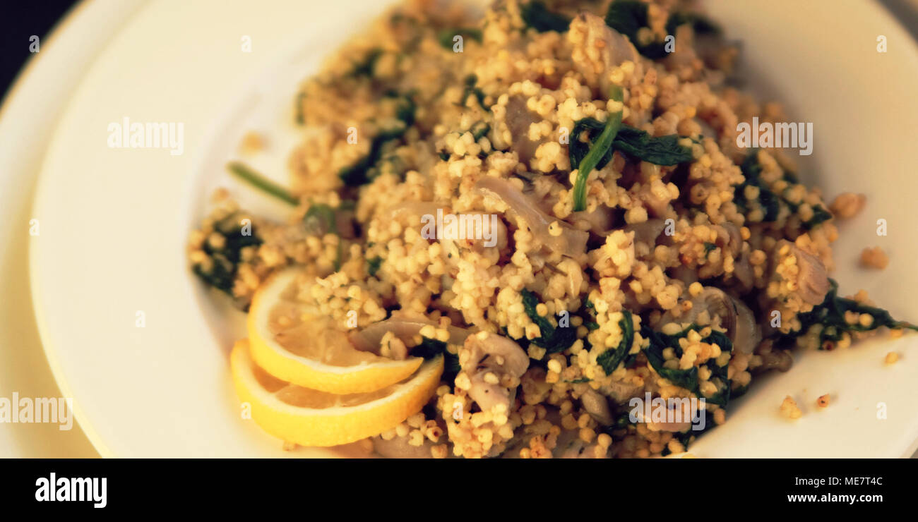 Hirse mit Pilzen und Spinat. Vegane Gerichte. Vegetarische couscous auf das runde weiße Platte. Breite Foto. Stockfoto