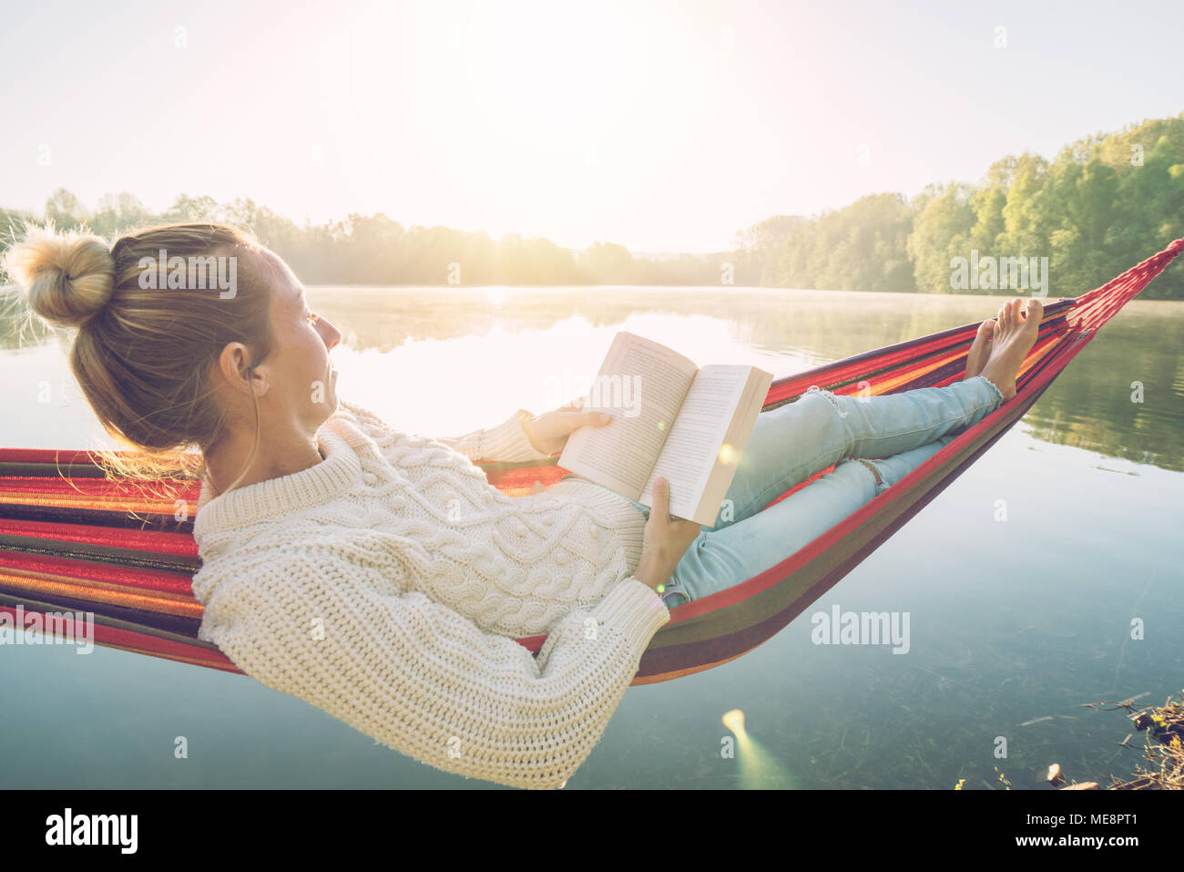 Junge Frau entspannen auf der Hängematte am See bei Sonnenaufgang, ein Buch zu lesen. Die Menschen reisen Entspannung Wohlbefinden Lernkonzept. Frankreich, Europa Stockfoto
