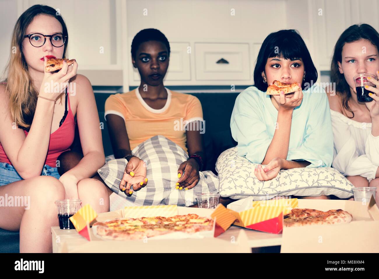 Eine vielfältige Gruppe von Frauen sitzen auf der Couch und essen Pizza zusammen Stockfoto