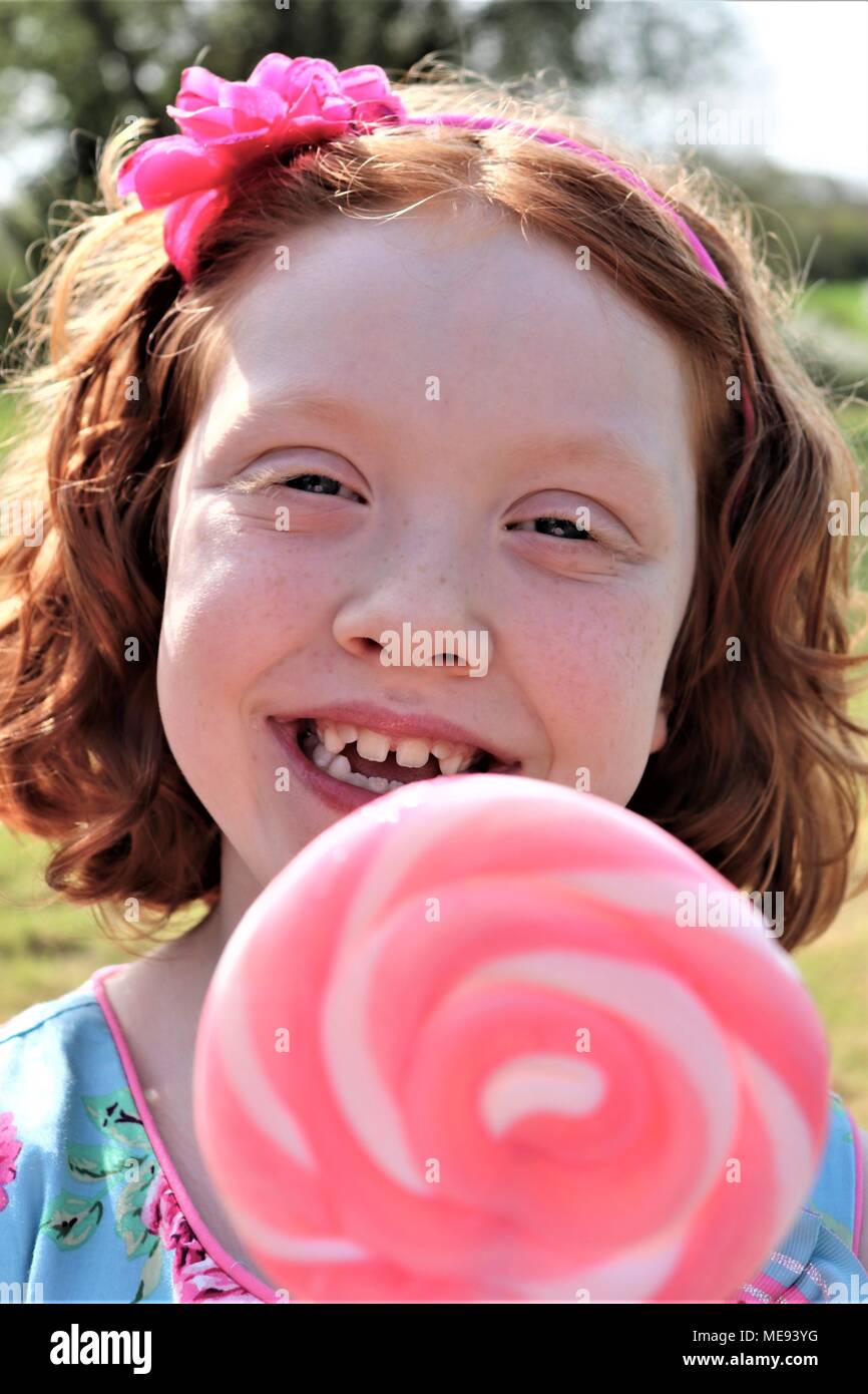 Eine rothaarige Behaarte Mädchen in ein schickes blaues Kleid mit einem großen, rosa und weißen Lollipop Stockfoto Eine rothaarige Behaarte Mädchen in ein schickes blaues Kleid mit einem großen, rosa und weißen Lollipop Stockfoto