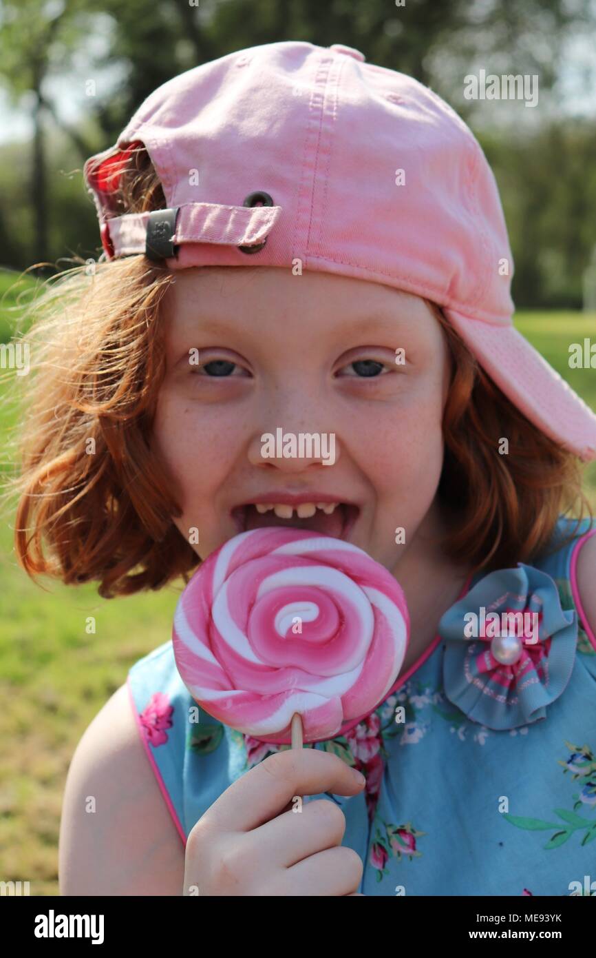 Eine rothaarige Behaarte Mädchen in ein schickes blaues Kleid mit einem großen, rosa und weißen Lollipop Stockfoto Eine rothaarige Behaarte Mädchen in ein schickes blaues Kleid mit einem großen, rosa und weißen Lollipop Stockfoto