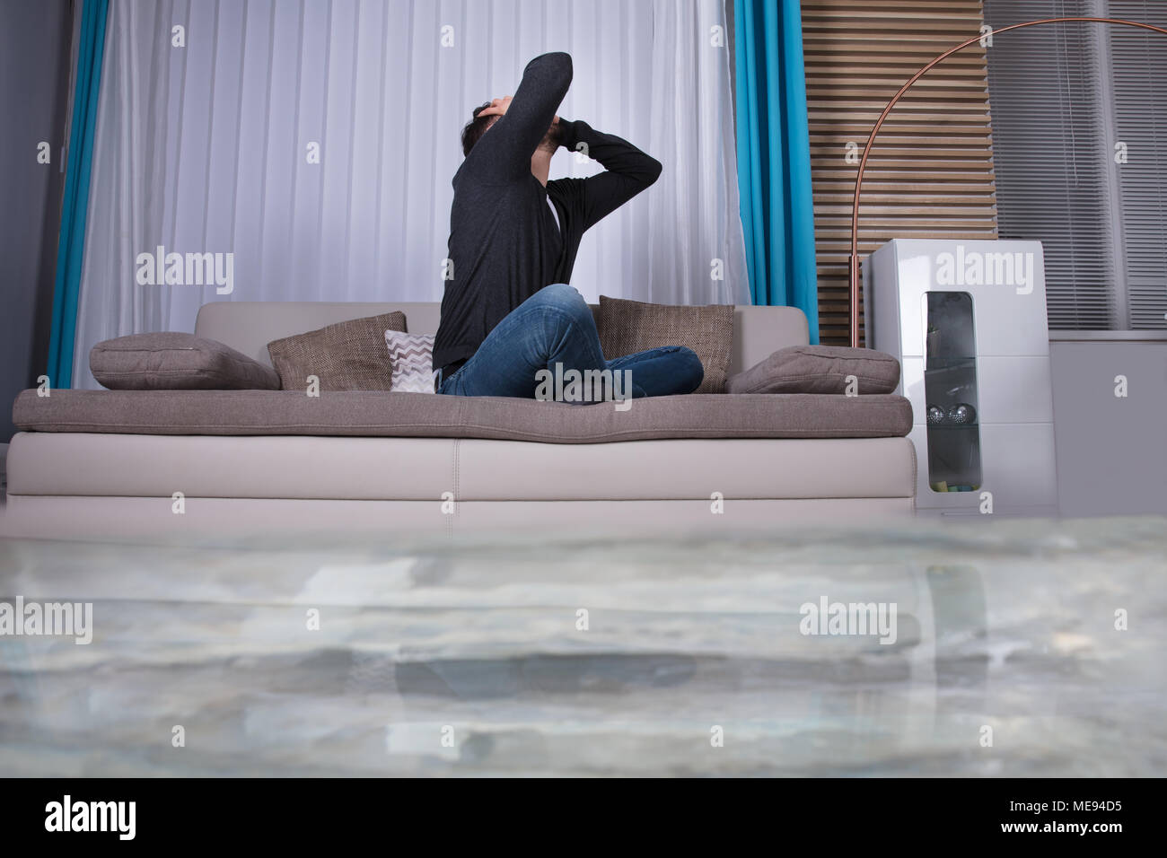 Mann auf Sofa mit Hände auf den Kopf Umkippen in Zimmer überflutet mit Wasser Stockfoto