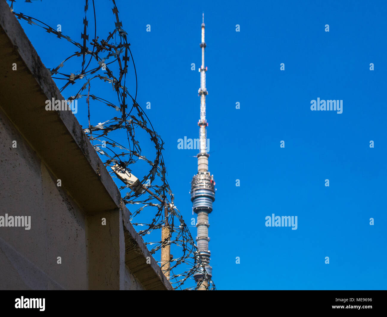 Ein grauer Beton Zaun mit Stacheldraht vor dem Hintergrund der Fernsehturm Ostankino an einem klaren, sonnigen Tag. Symbolisiert die Beschränkung der fre Stockfoto