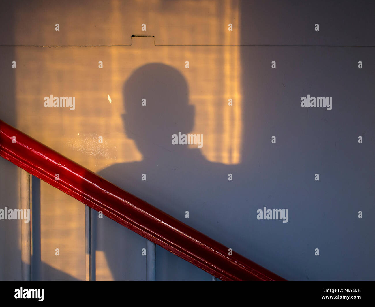 Der Schatten der Mann von der Abendsonne auf der Wand des Treppenhauses vor dem Hintergrund der Geländer. Zeichnung aus dem alten Glas an der Wand. Stockfoto
