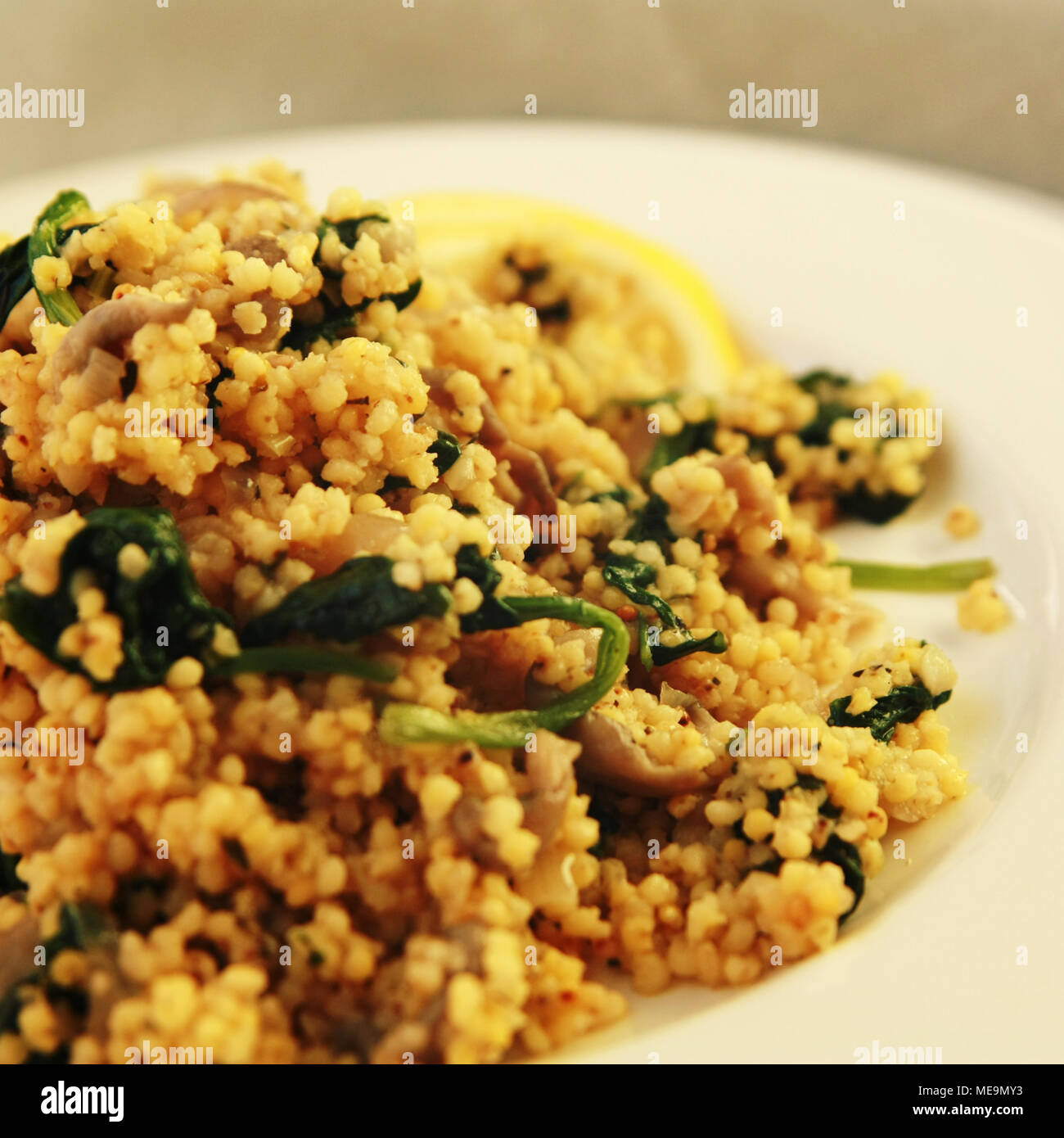 Hirse mit Pilzen und Spinat. Jüdische Küche. Vegetarische couscous auf das runde weiße Platte. Close Up. Getönten Foto. Stockfoto