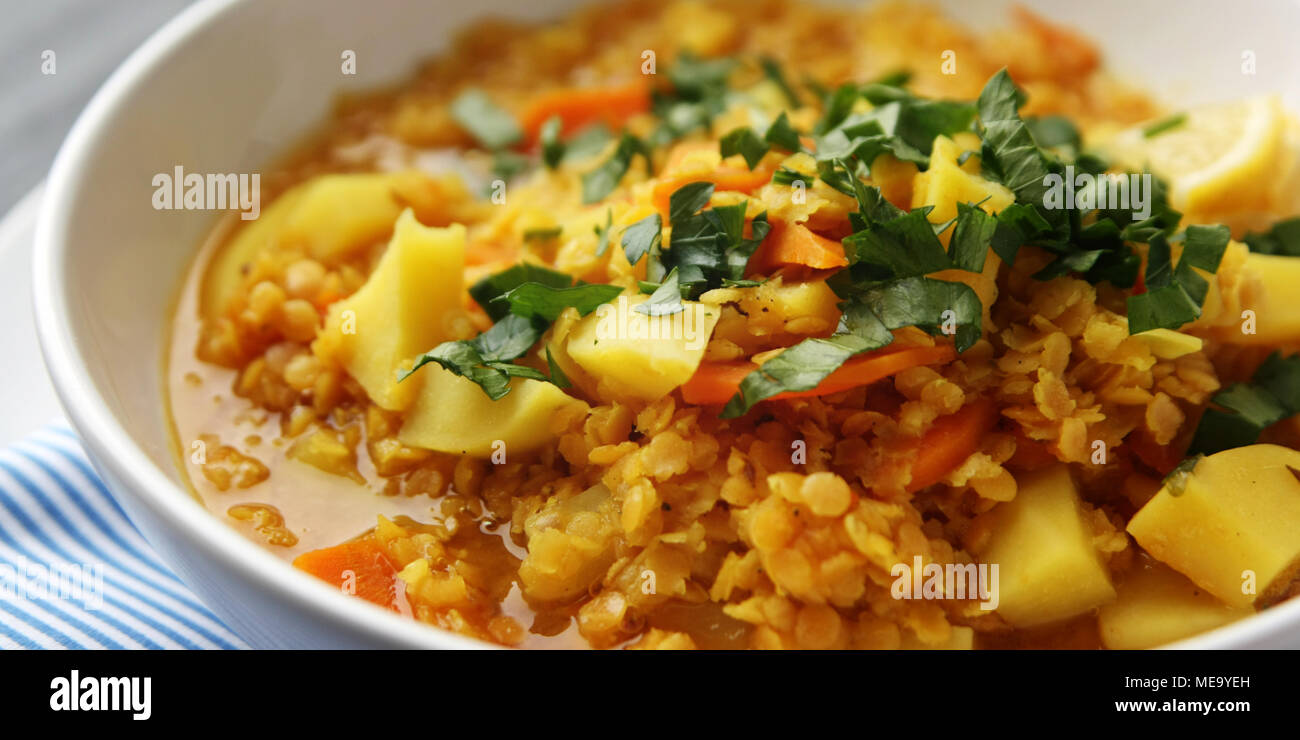 Rote Linsen Eintopf mit Kartoffeln, Karotten und Kurkuma. Getönten Foto. Gesundes Mittagessen auf der Runde weiße Platte. Bunte veganes Gericht mit Kartoffeln, Karotten und Tur Stockfoto