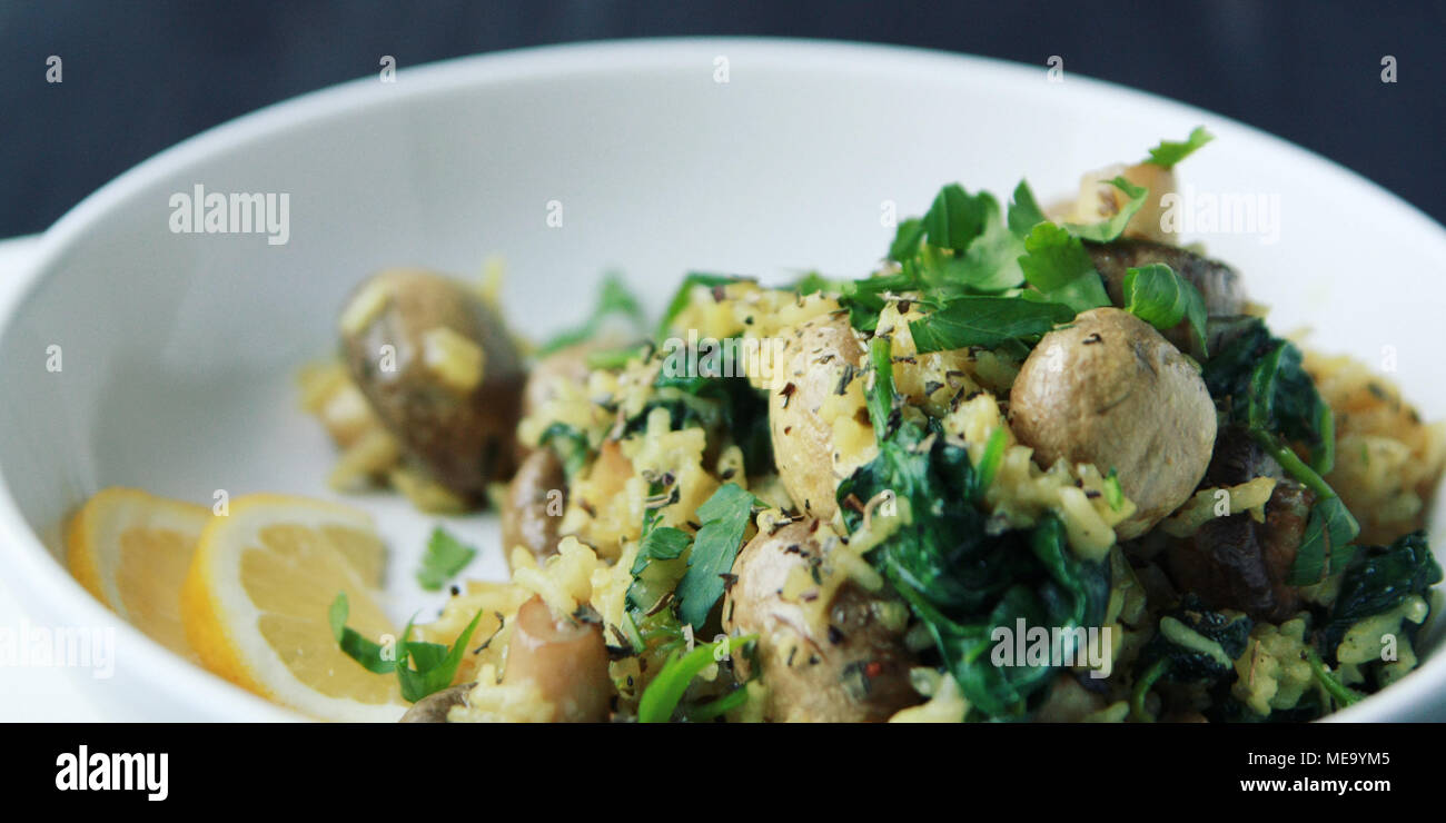 Gelber Reis mit Pilzen und Spinat. Vegane Gerichte. Europäische Küche. Vegetarische Gelbwurz Reis in die weiße Schüssel. Fleischlos. Breite Foto. Stockfoto
