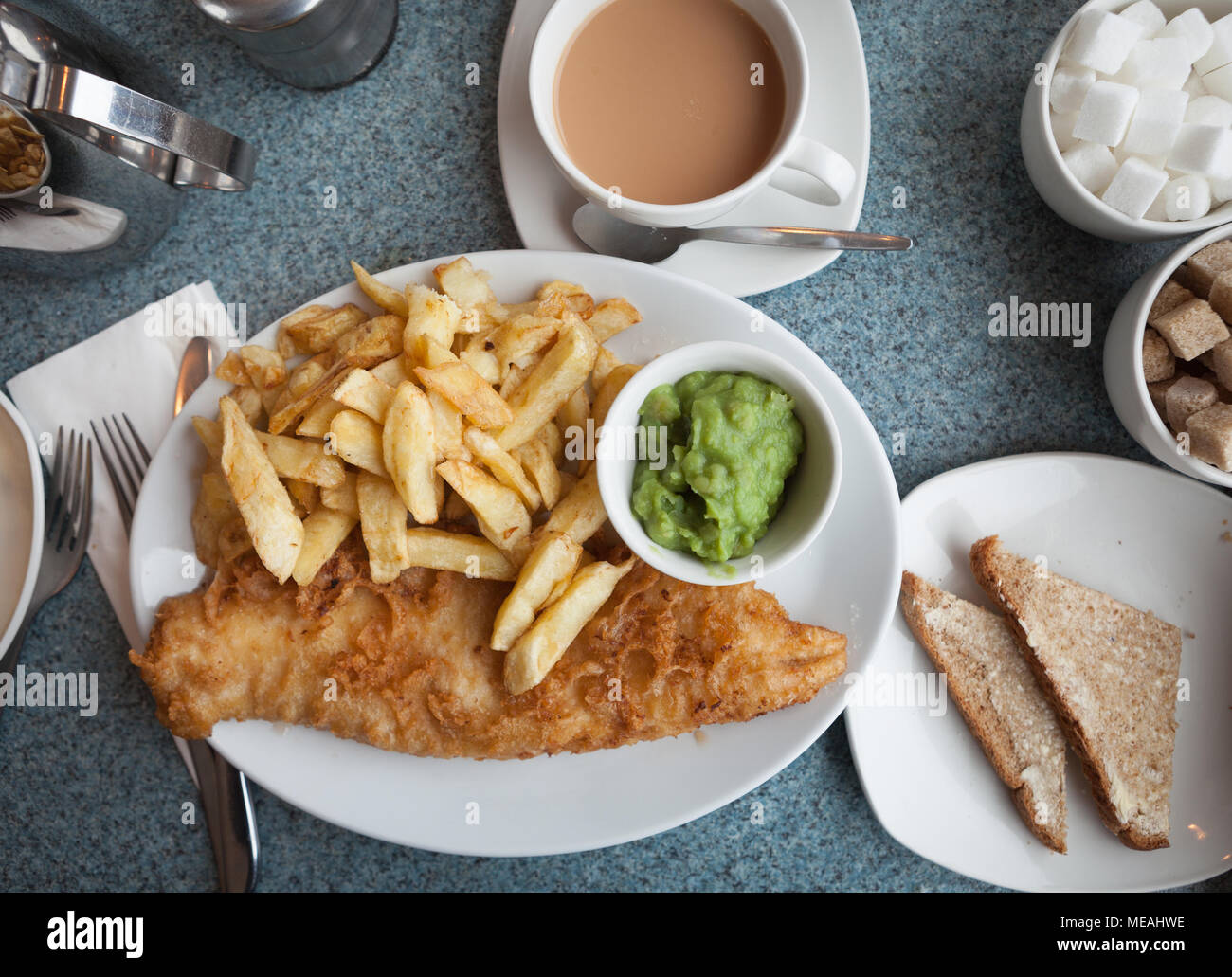 Authentische britische Fish und Chips, mit Erbsenpüree, Butterbrot und einer Tasse Kaffee Stockfoto